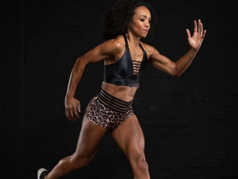 Melissa Neill in a dynamic sprinting pose, wearing a black sports top and leopard-print shorts against a dark background.