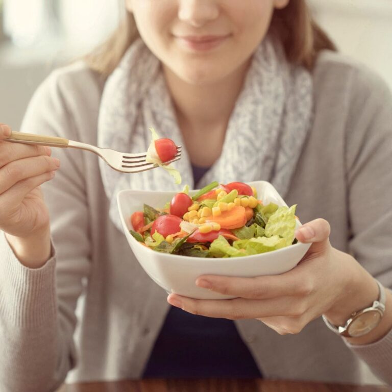 A woman enjoying a fresh salad with cherry tomatoes, lettuce, carrots, and corn.