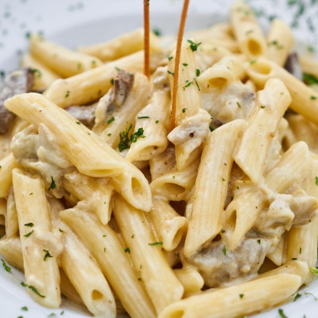 A close-up of creamy mushroom penne pasta garnished with fresh herbs.