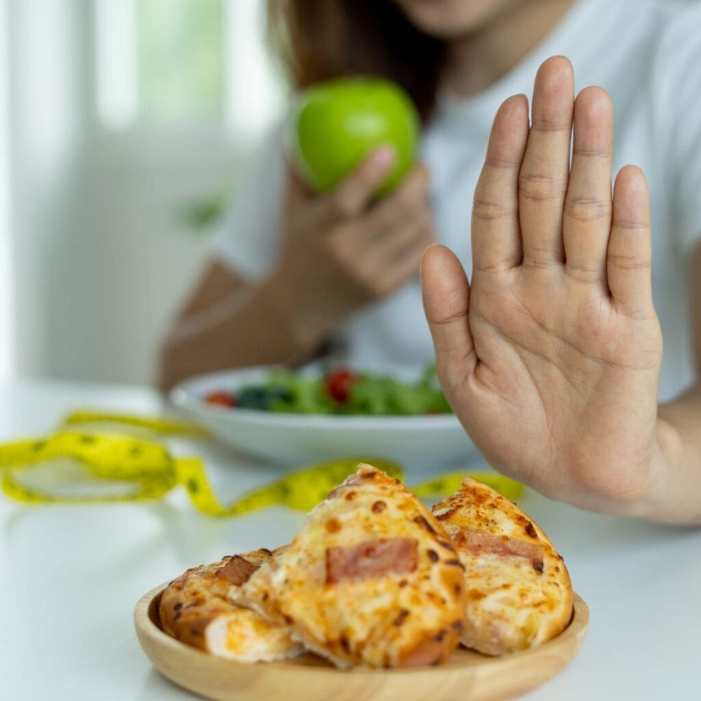 A woman holding up her hand to refuse pizza while eating a healthy salad and an apple.