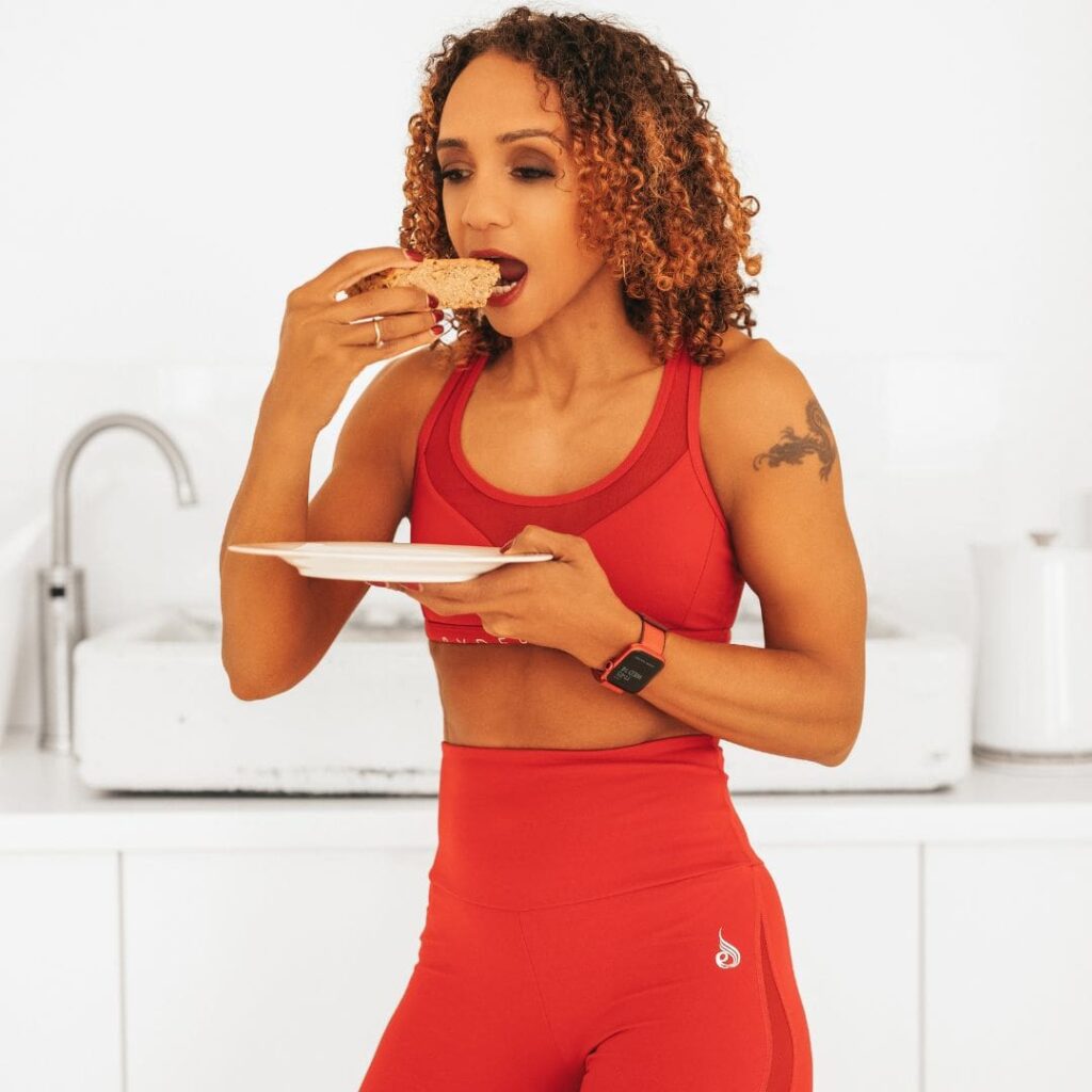Melissa Neill wearing a red sports outfit, enjoying a healthy meal in a bright kitchen.