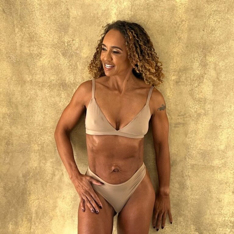 Melissa Neill posing in a nude-colored bikini against a gold-toned background, showcasing her toned physique and confidence.