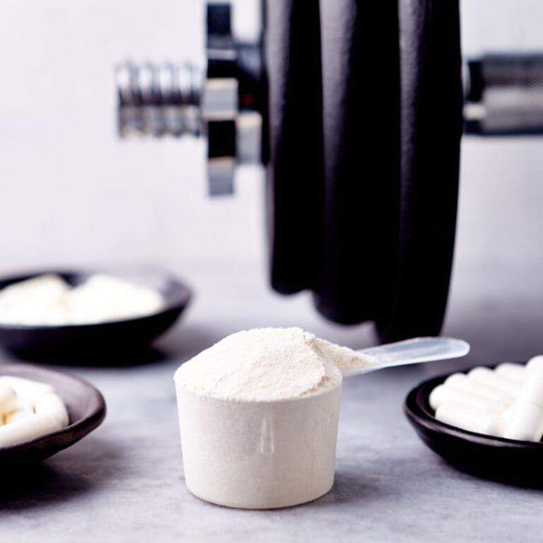 A scoop of creatine powder with weight plates and capsules in the background.